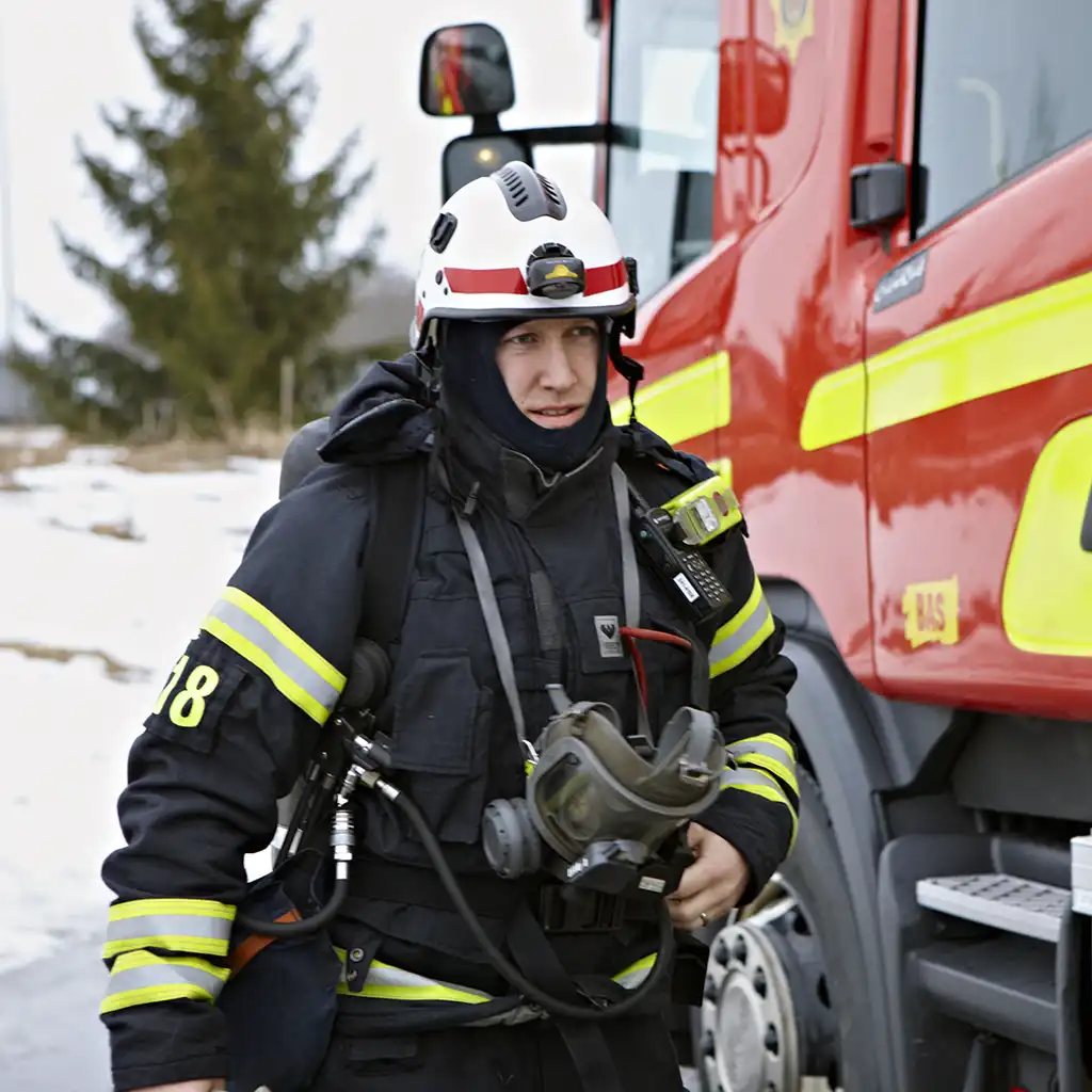 Bild på en brandman som kommer gående mot kameran med en brandbil i bakgrunden.