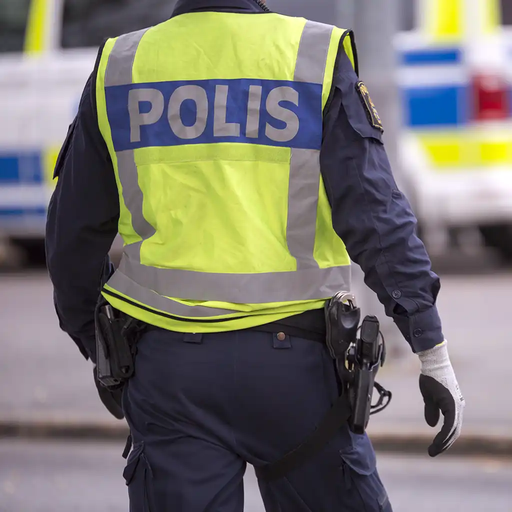 Ryggtavlan på en polis med en polisbil synlig i bakgrunden.