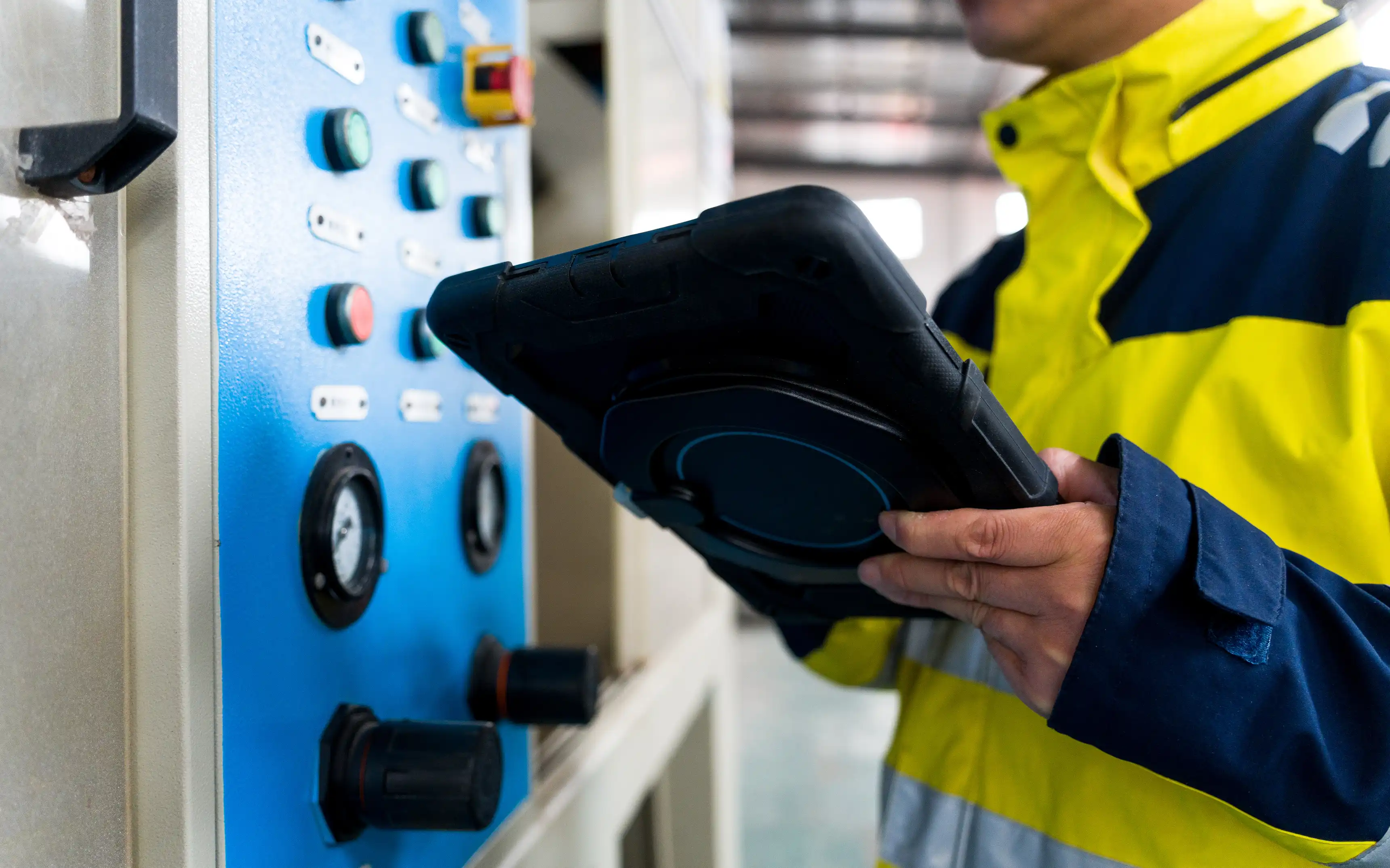 Bild på en industriarbetare som kontrollerar en maskin med en ruggad surfplatta i handen.