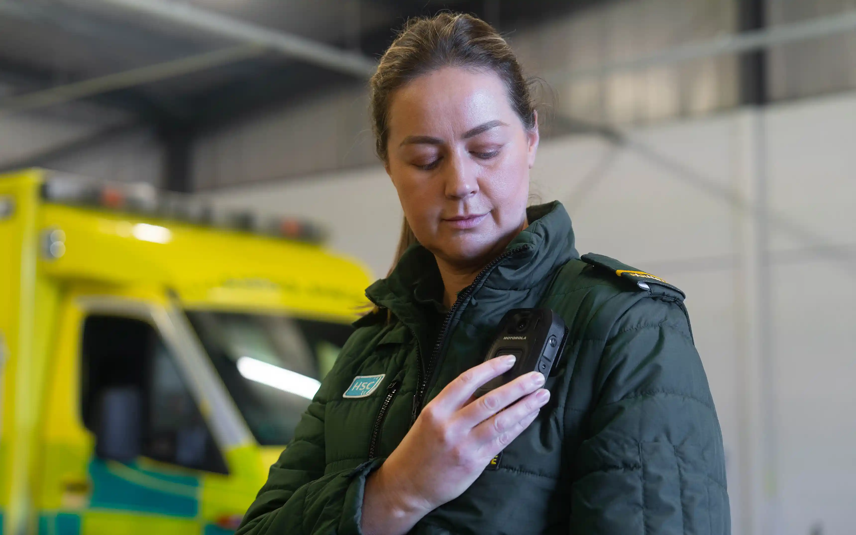 Kvinnlig ambulanssjukvårdare som i operativ arbetsmiljö som aktiverar kroppsburen kamera manuellt.