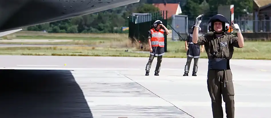 En militär som står och dirigerar ett transportflyg på en flygflottilj med en stor kommunikationsheadset på huvudet..