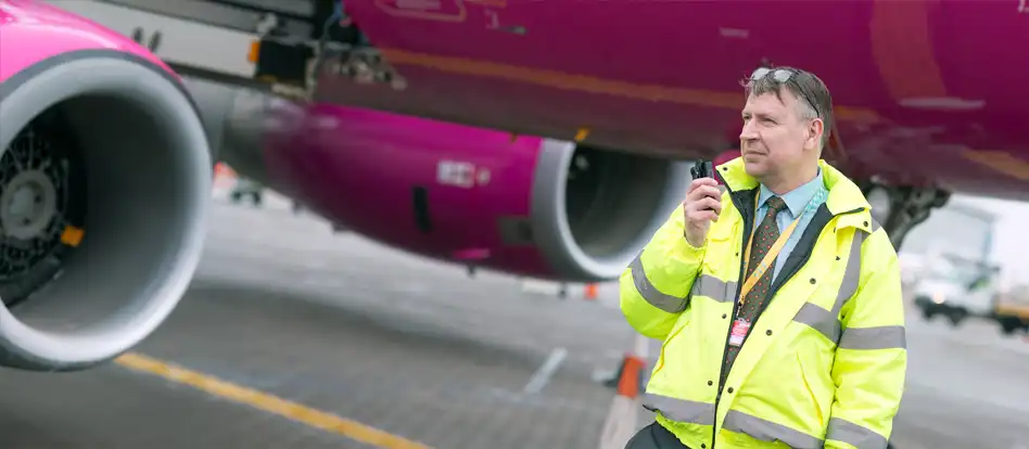 En flygplatsmedarbetare som pratar i en Tetra-terminal med ett rosa jetplan i bakgrunden.